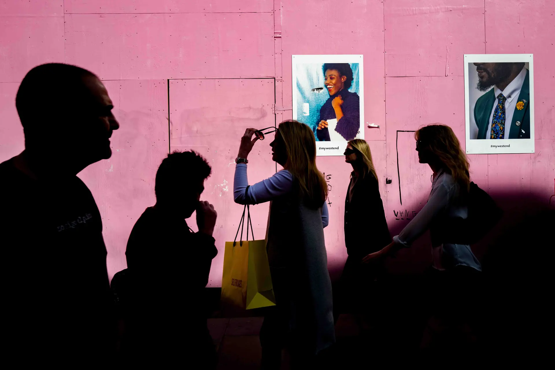 People walking past a pink-coloured wall