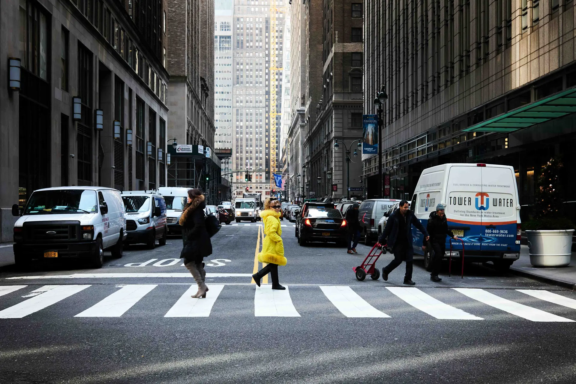 Woman in a yellow winter coat crosses a zebra crossing between tower blocks