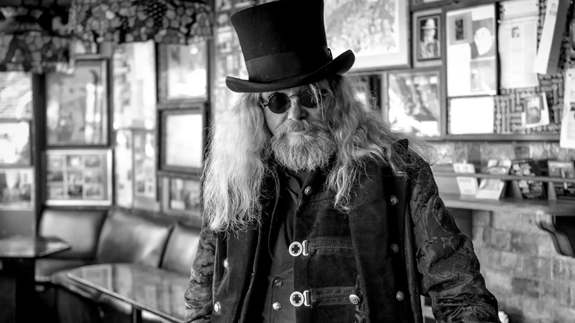 Old rocker with long hair, sunglasses and top hat in a pub, black and white picture