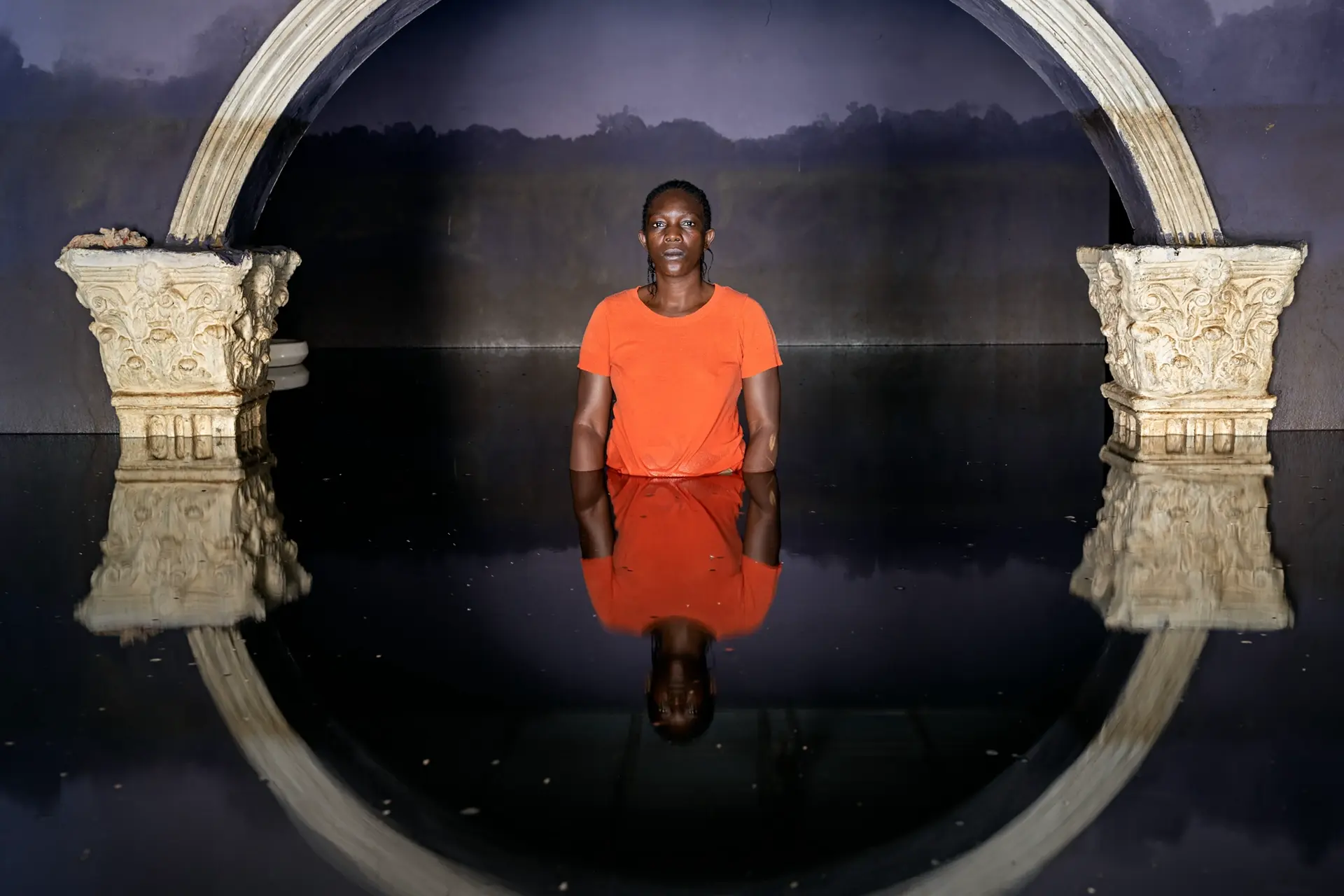 A man standing in the water below an arch that is reflected in the water.