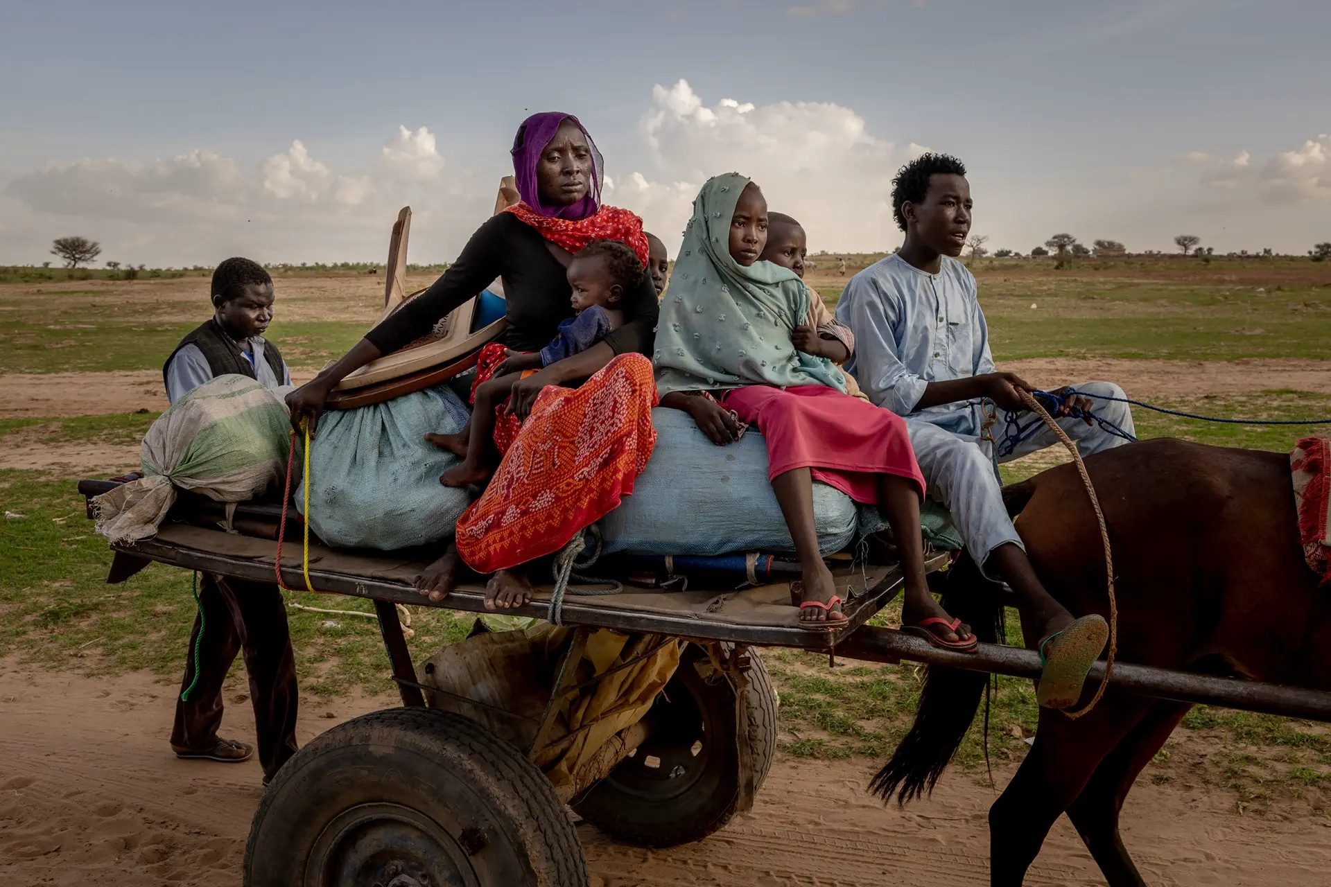A woman and three children sitting on a cart pulled by a horse.
