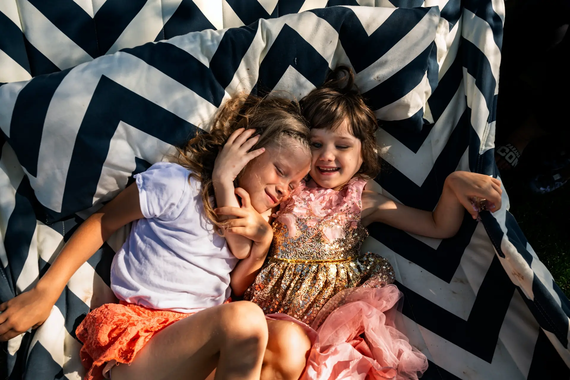 Two little girls lie loughing in a hammock.
