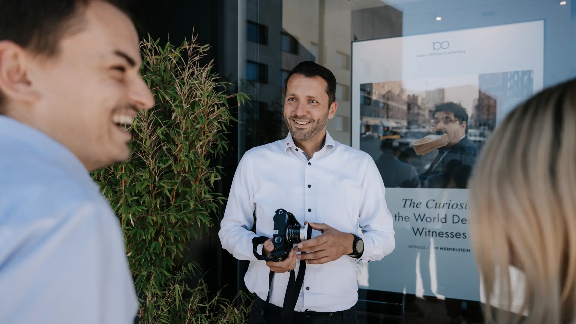 Leica Community standing in a circle with a Leica camera and laughing