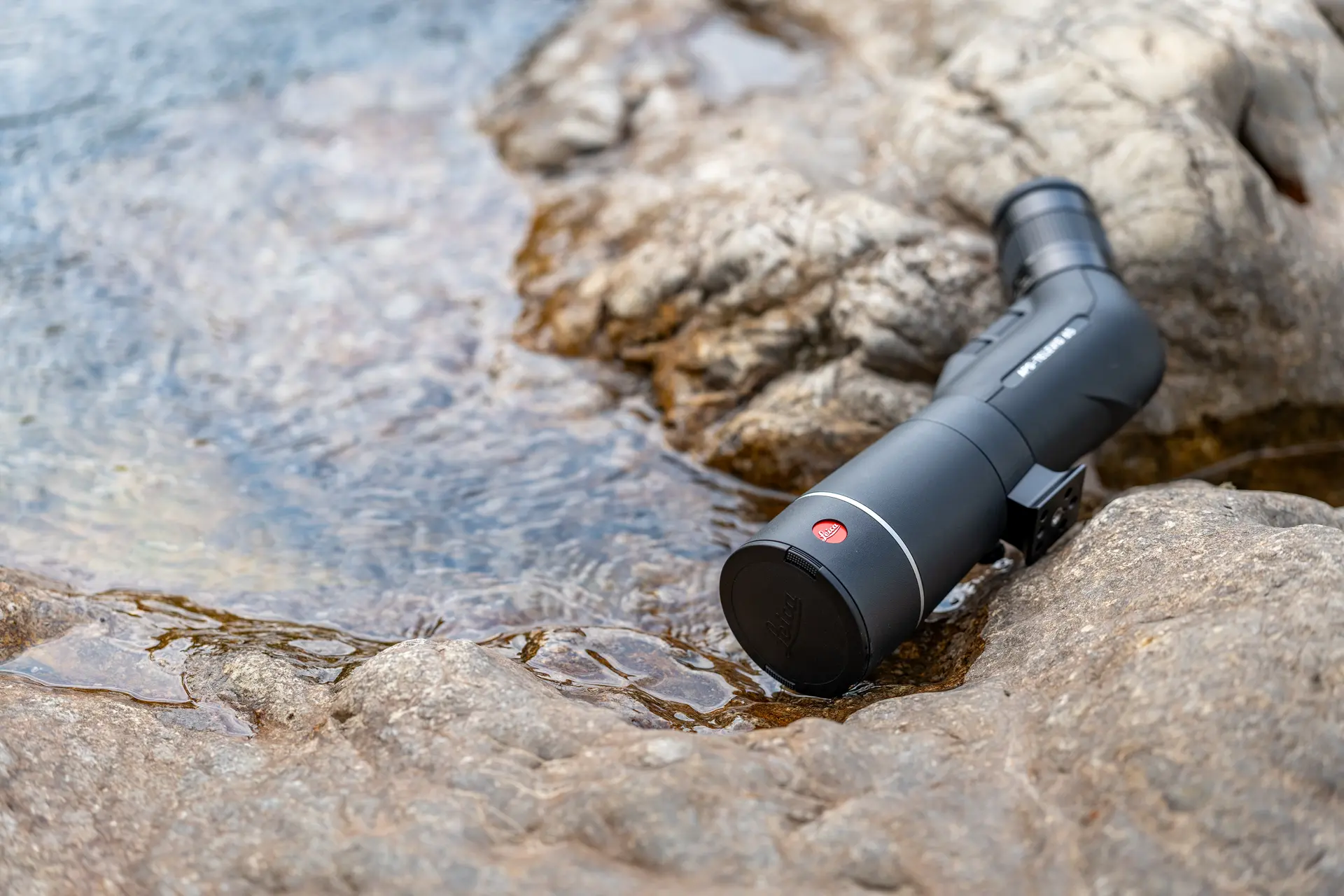 Leica APO-Televid 65 spotting scope is lying in a puddle on a rock