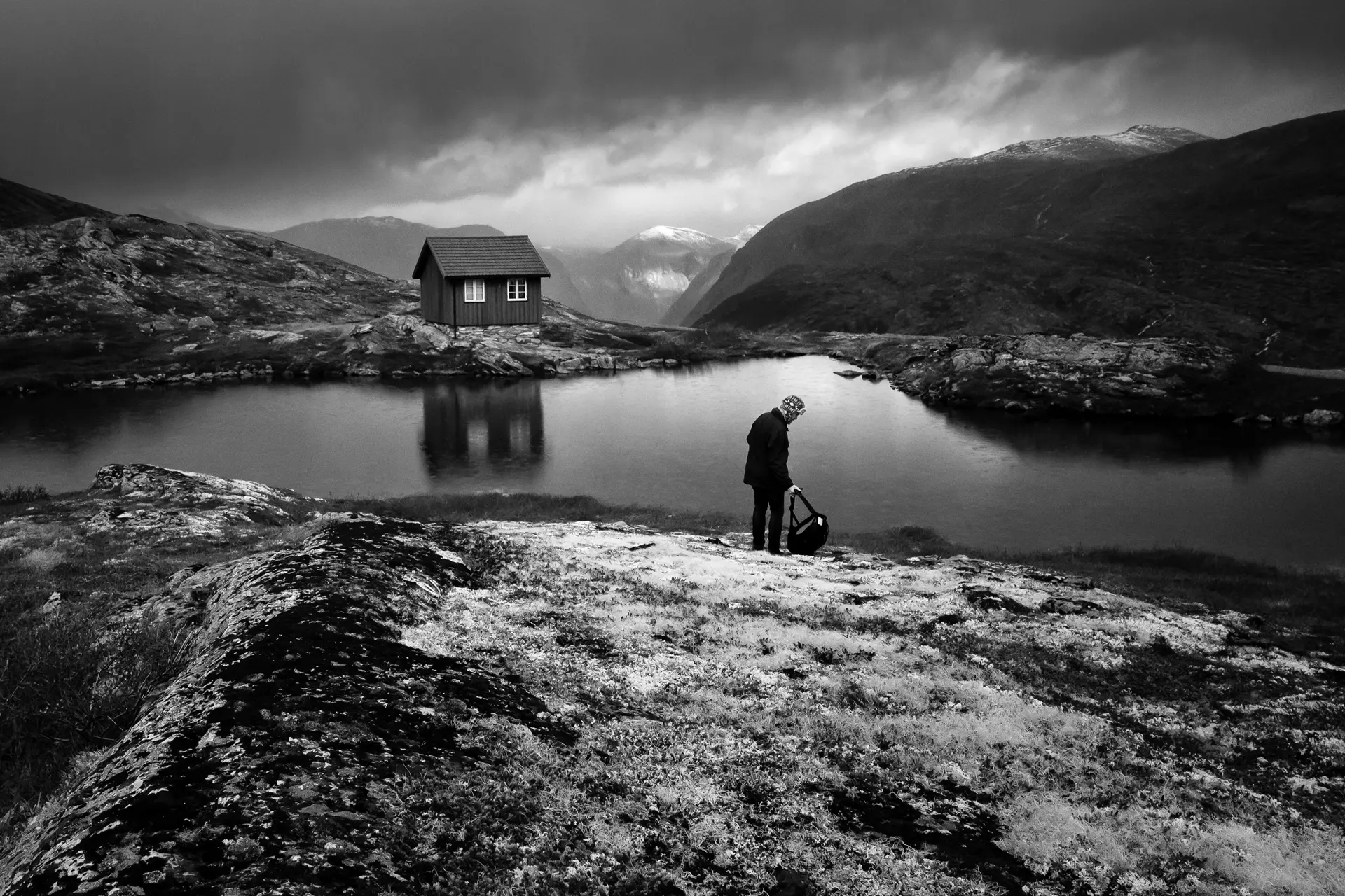Old man at a mountain lake where there is a small hut