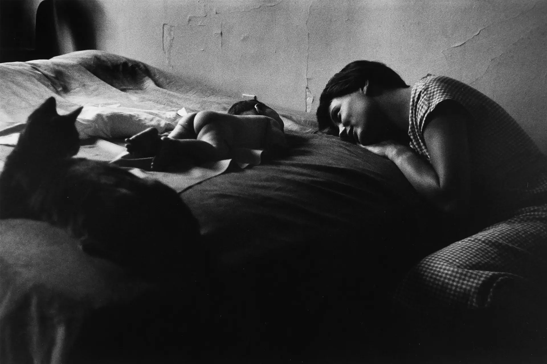 A woman lies on the bed and gazes dreamily at her naked baby a cat lies next to them