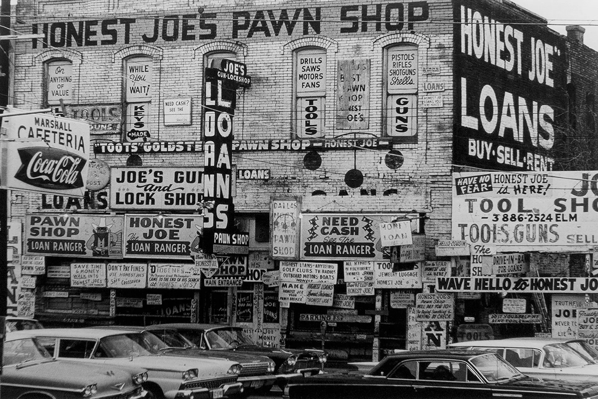 Six vintage cars in front of an old building with lots of advertising signs, black and white photograph