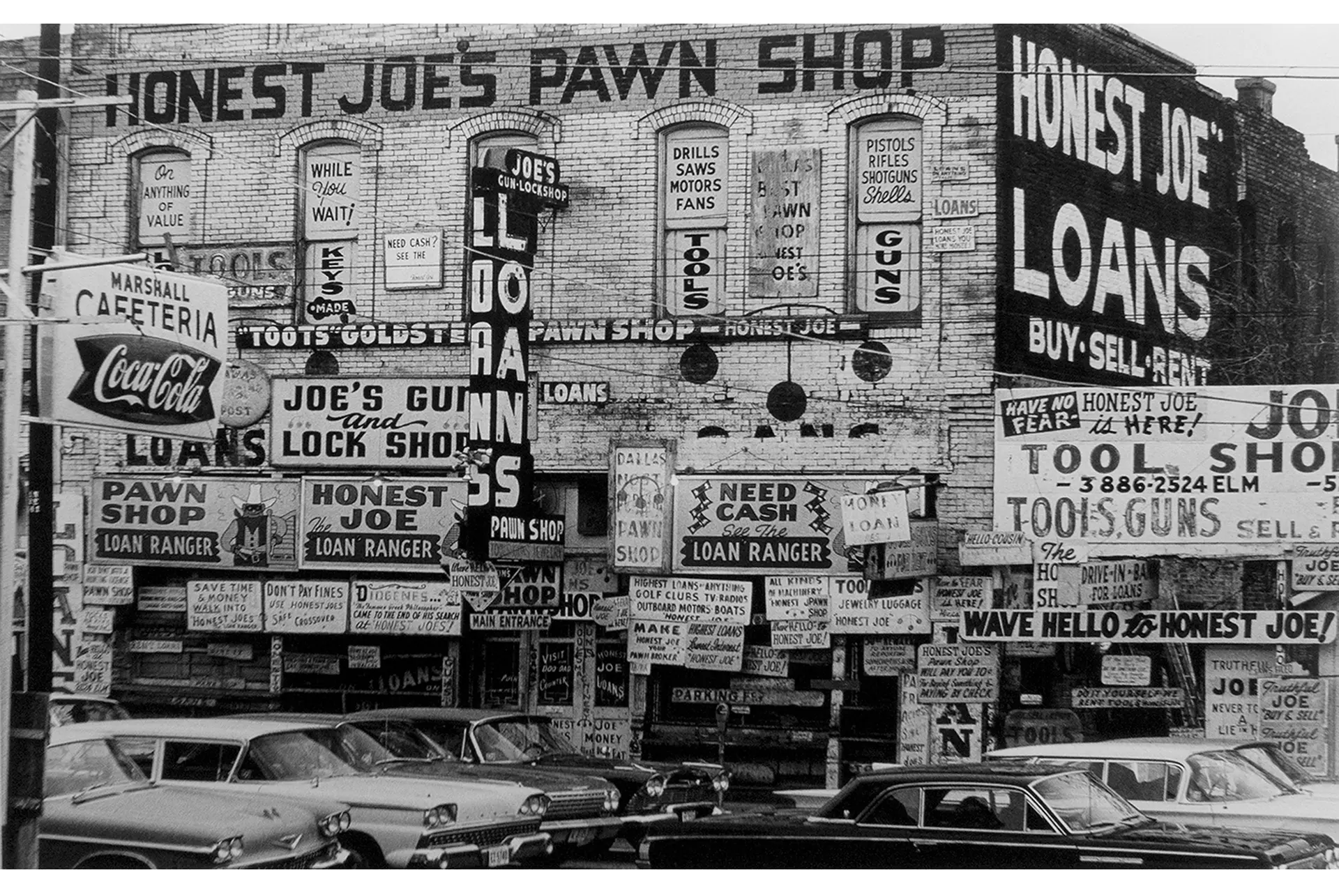 Six vintage cars in front of an old building with lots of advertising signs, black and white photograph