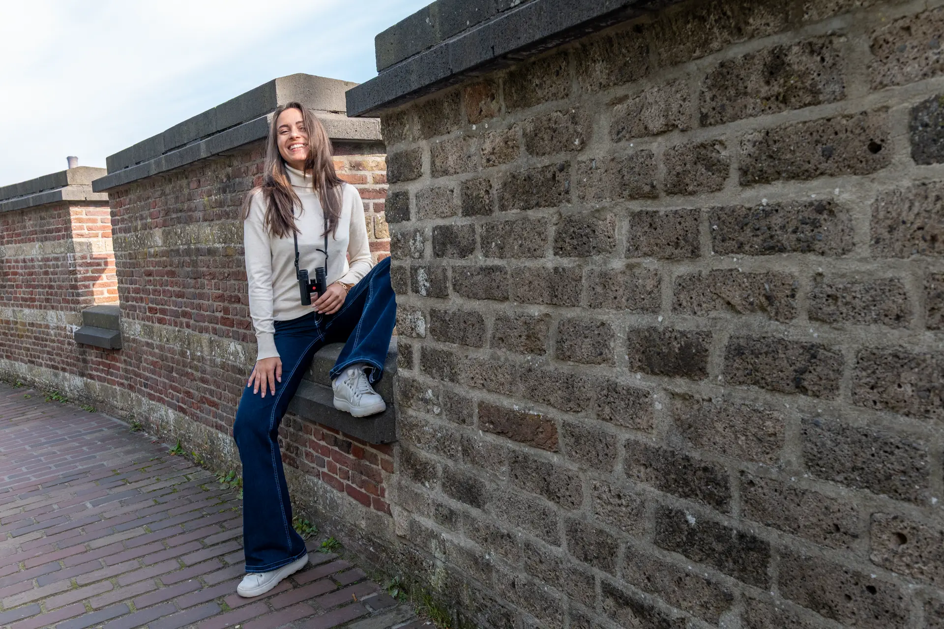 Woman sitting on a wall with her Leica Noctivid Compact