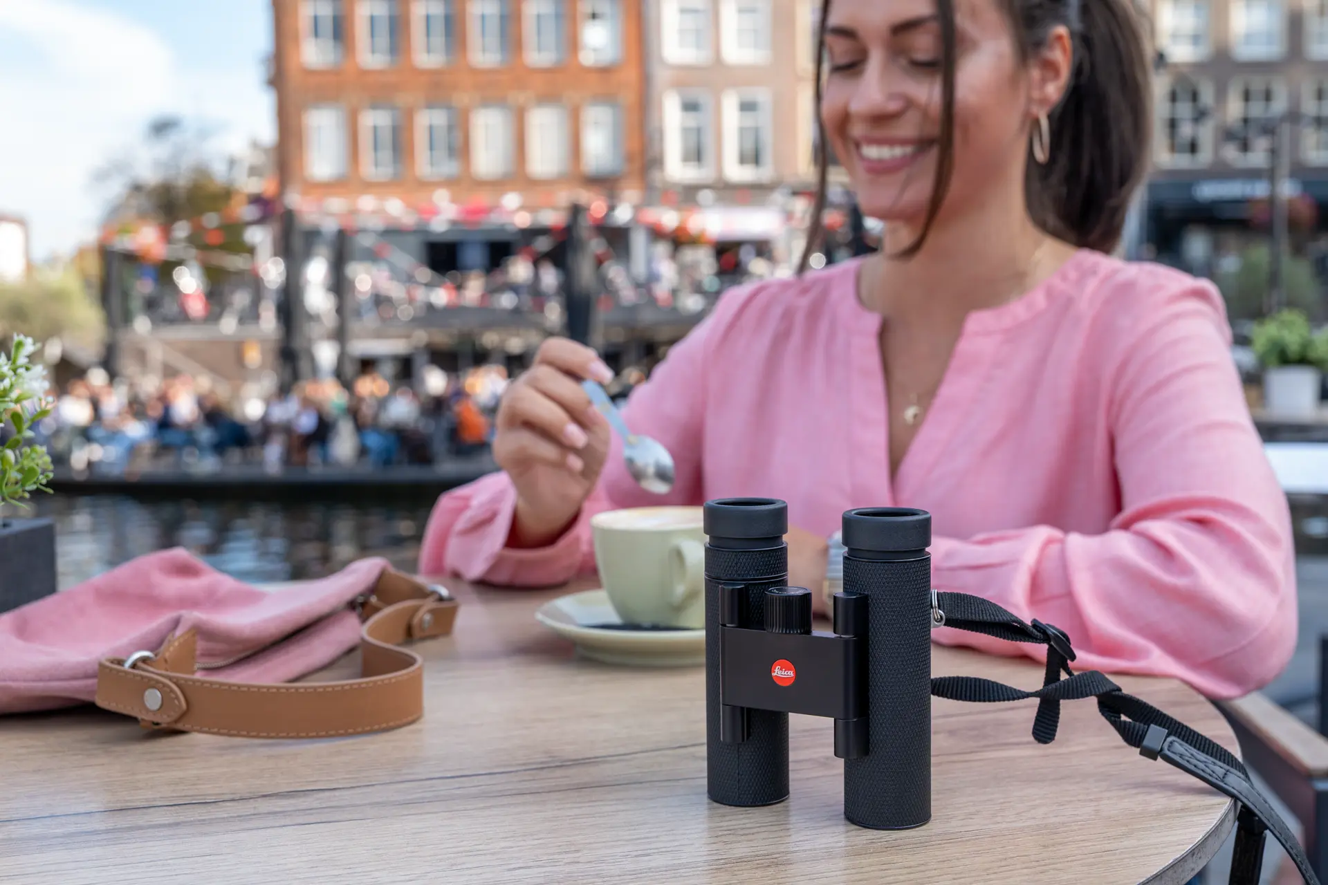Woman sitting in a cafe with her Leica Noctivid Compact next to her