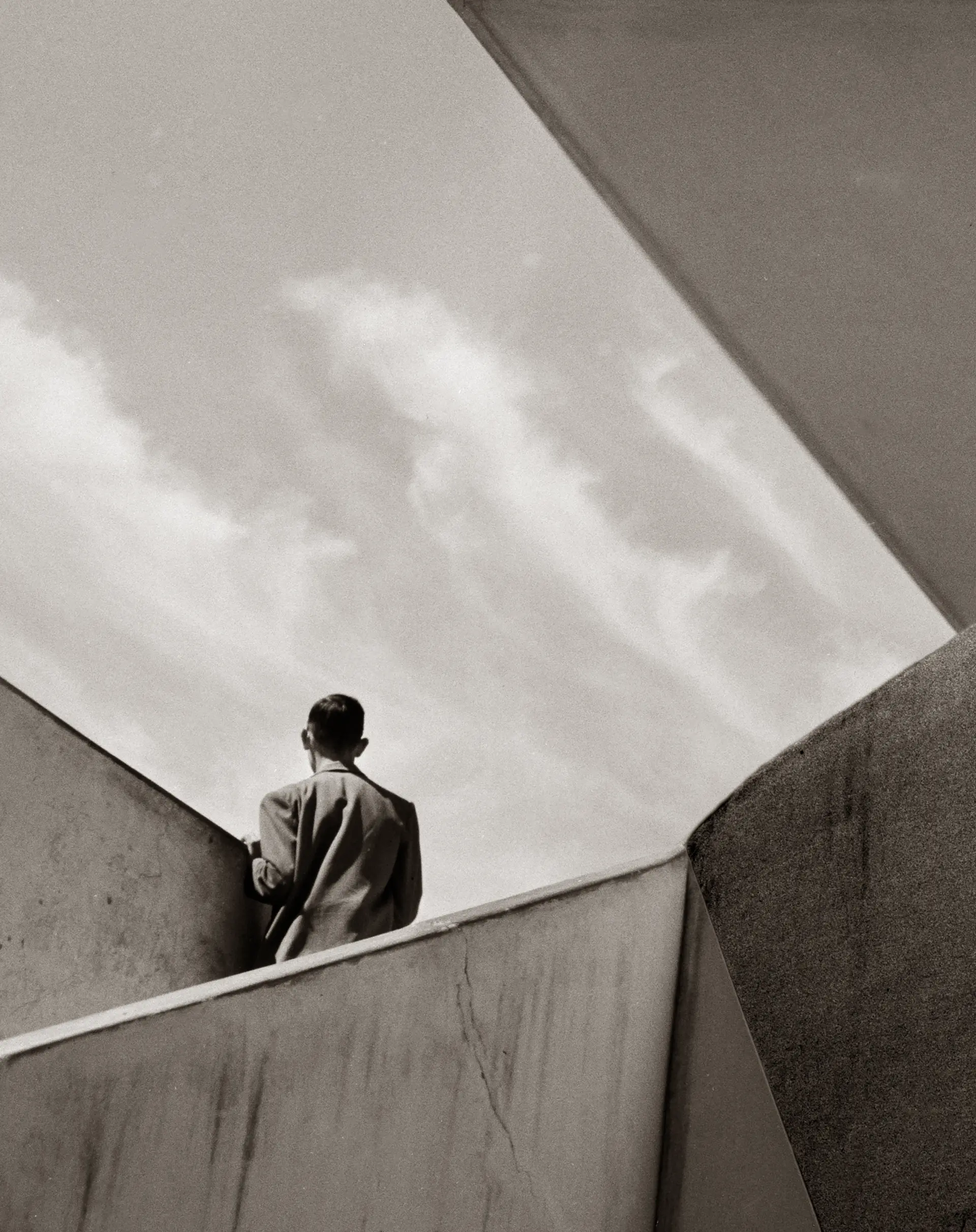 Black and white photo of a man, standing in a stone building and only seen from behind and afar