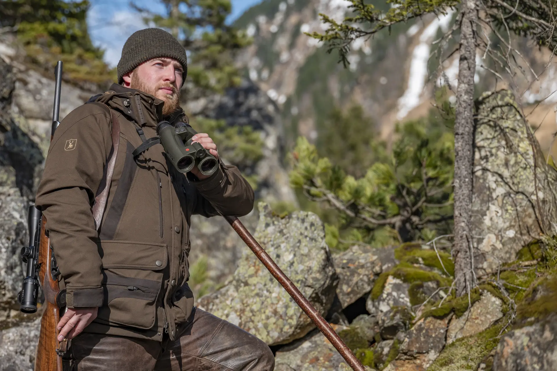 Man in the mountain using his Leica geovid Pro in olive green