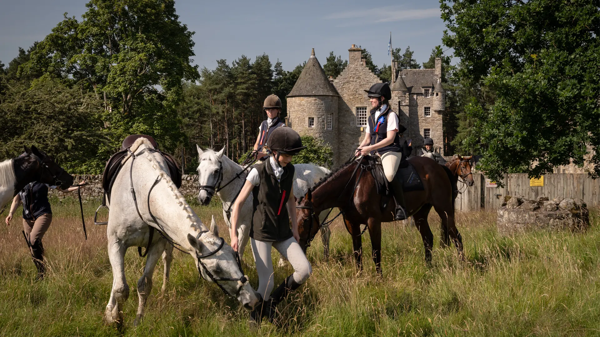 Horses and riders in front of an old scottish castle