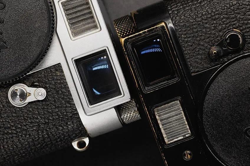 A silver and Black vintage cameras showing their rangefinder.