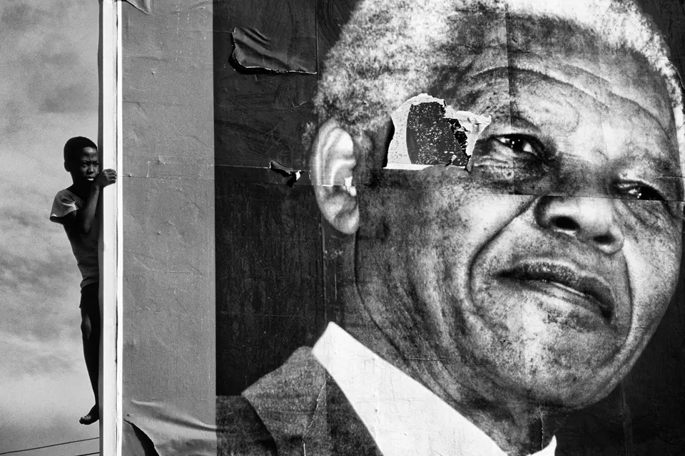 Image taken by Tom-Stoddart, supporter at ANC rally in South Africa peer behind a sign bearing the image of their President Nelson Mandela