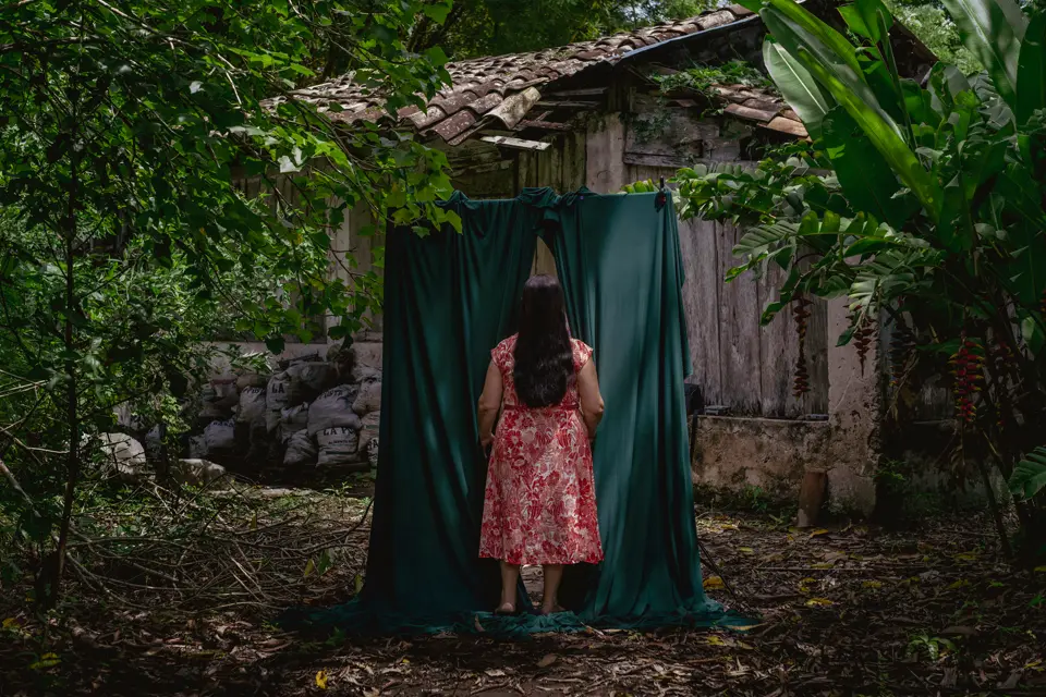 Woman standing in front of green cloak in forest with forest house