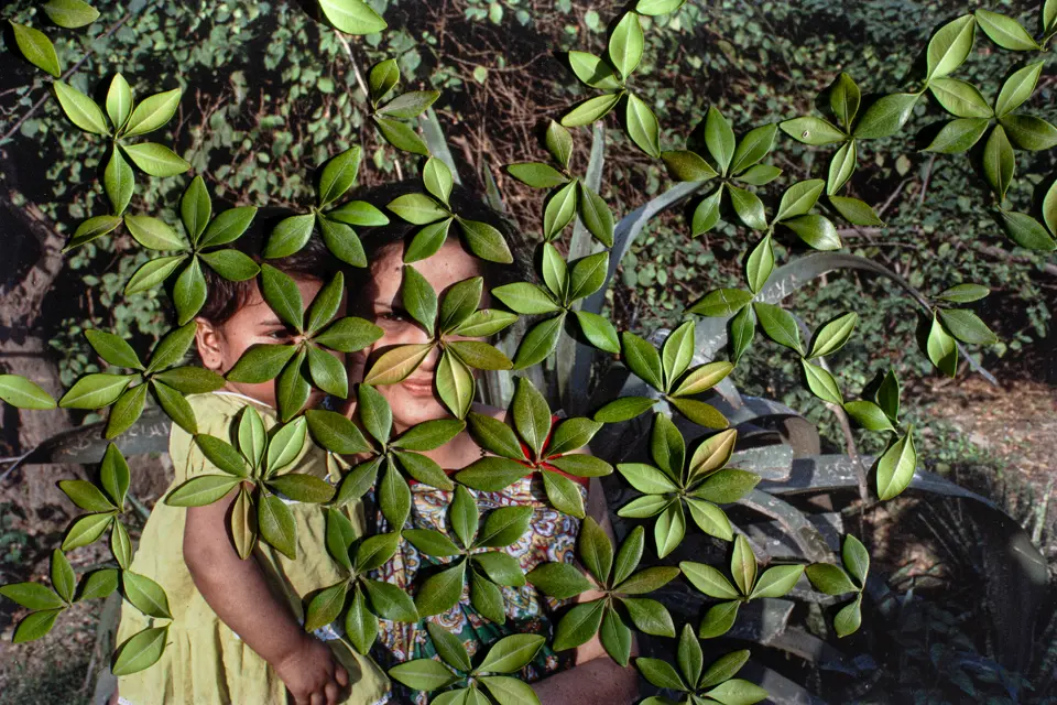Woman with baby in arms stands behind leaves