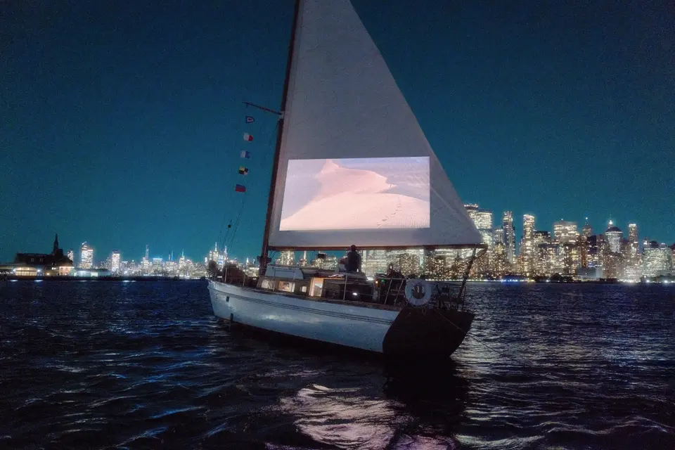 a few people watch a film on the sail of a sailboat on the water