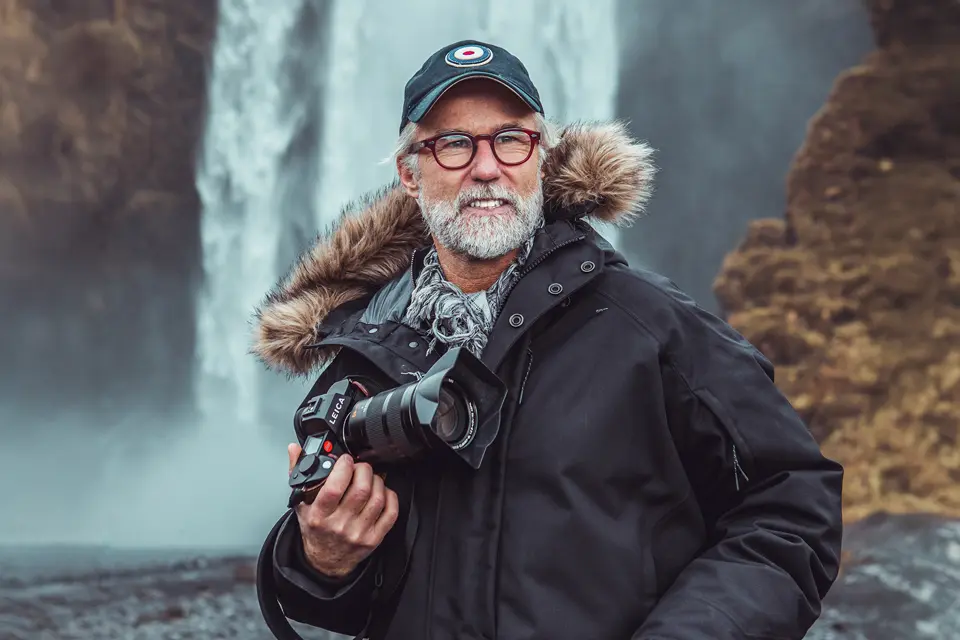 Photographer Ragnar Axelsson with a Leica Camera in front of a waterfall