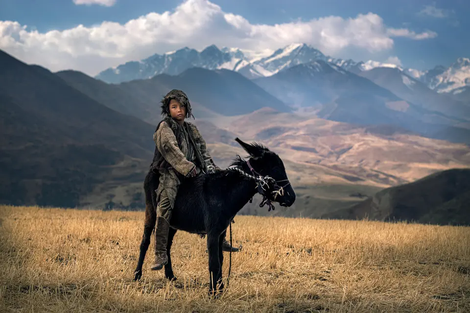 Little Kyrgyz Nomad on his donkey in front of moutains