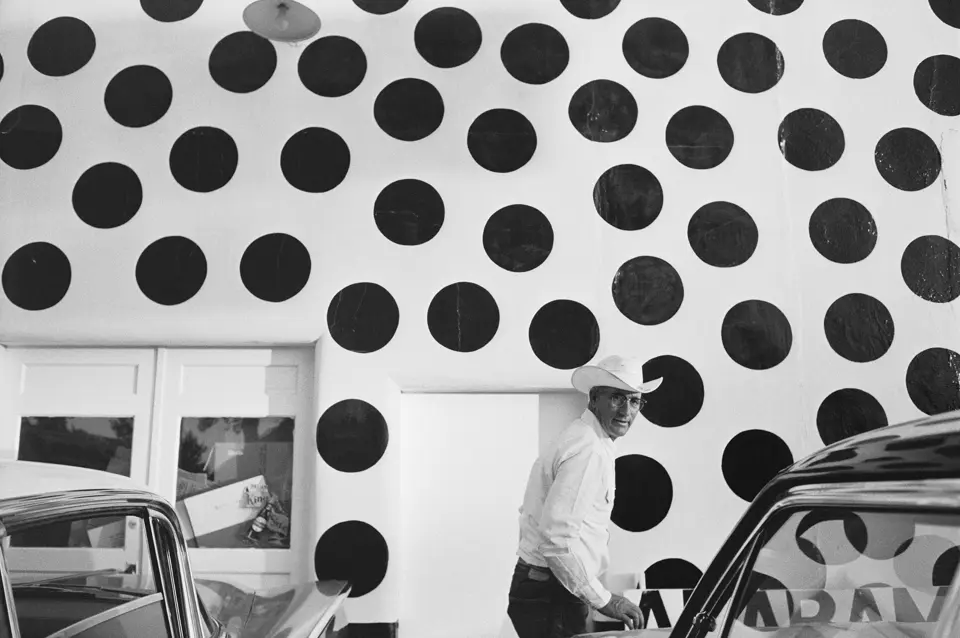 Man with hat in front of a white wall with large black dots