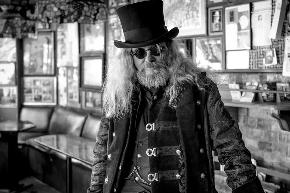 Old rocker with long hair, sunglasses and top hat in a pub, black and white picture
