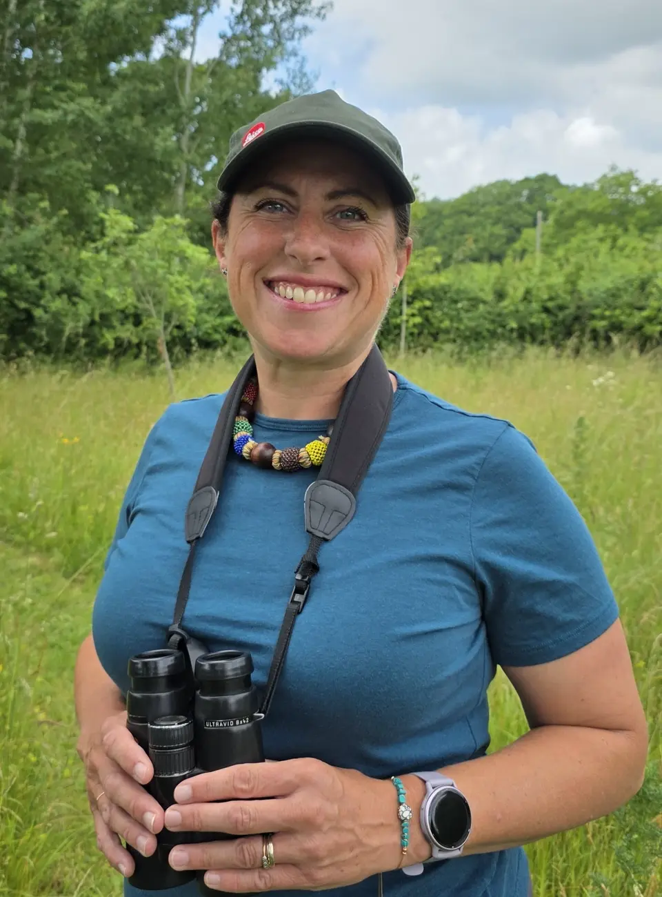 Image of Penny Green holding a pair of binoculars in front of a field of green.