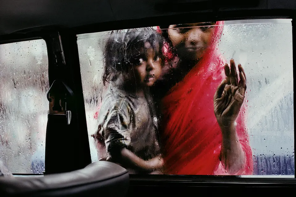 Poor woman with a child in her arms looking into a car from the outside