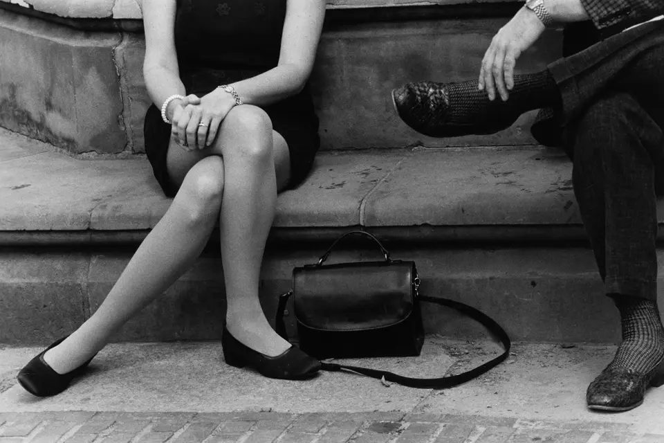 A man and a woman dressed elegantly are sitting on a stone bench only their lower bodies are visible