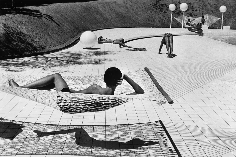 A place where a boy is lying in a hammock in the foreground in the background, you can see a woman sunbathing and a man doing sports