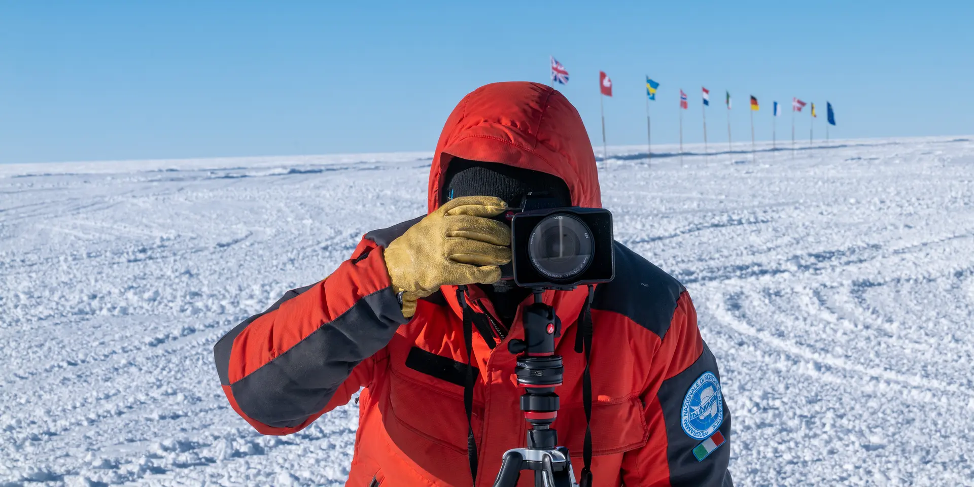 Person takes a photo in a snowy landscape with European flags in the background.