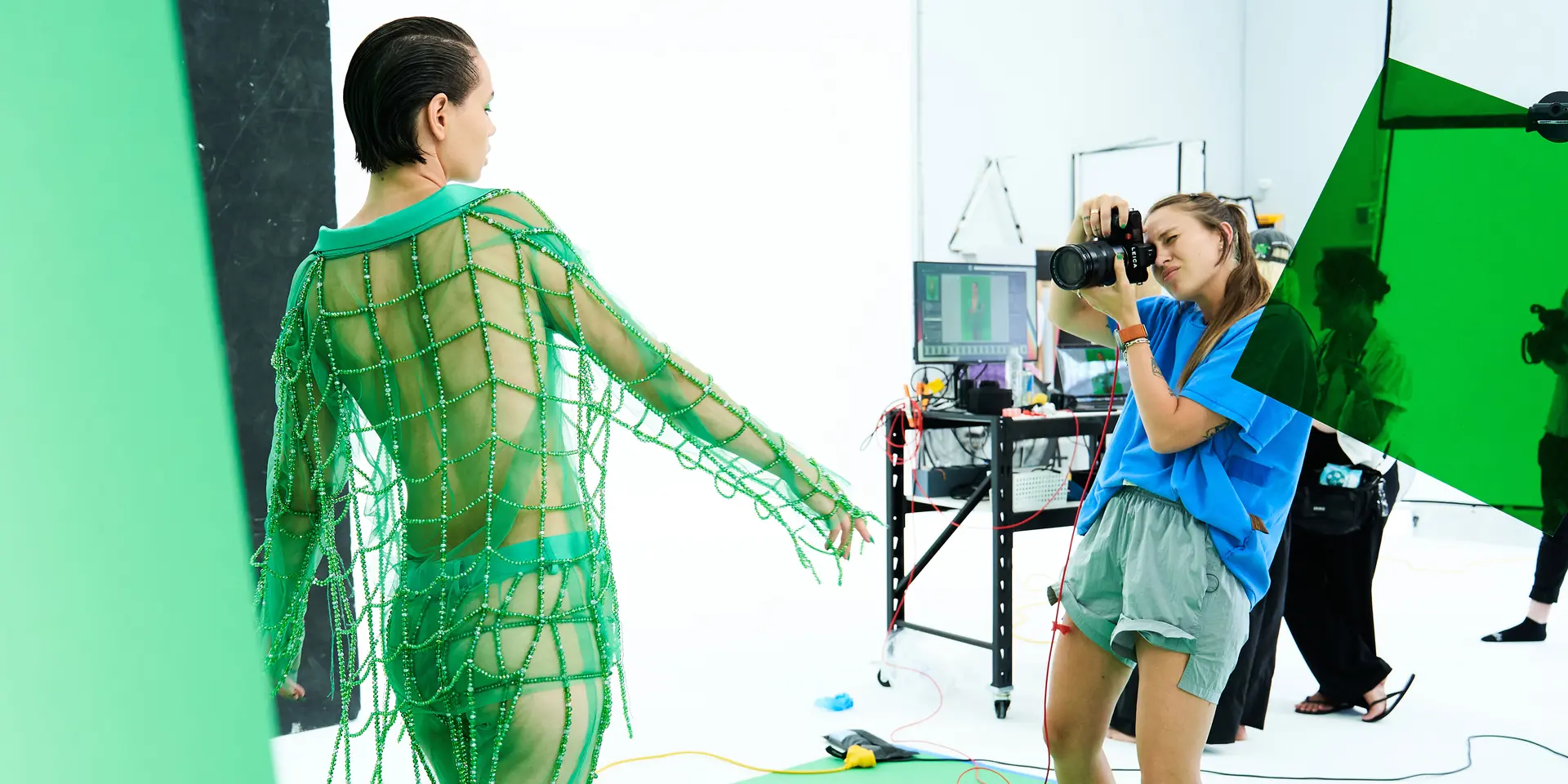 Photographer takes a picture in a studio of a model in a green net outfit.