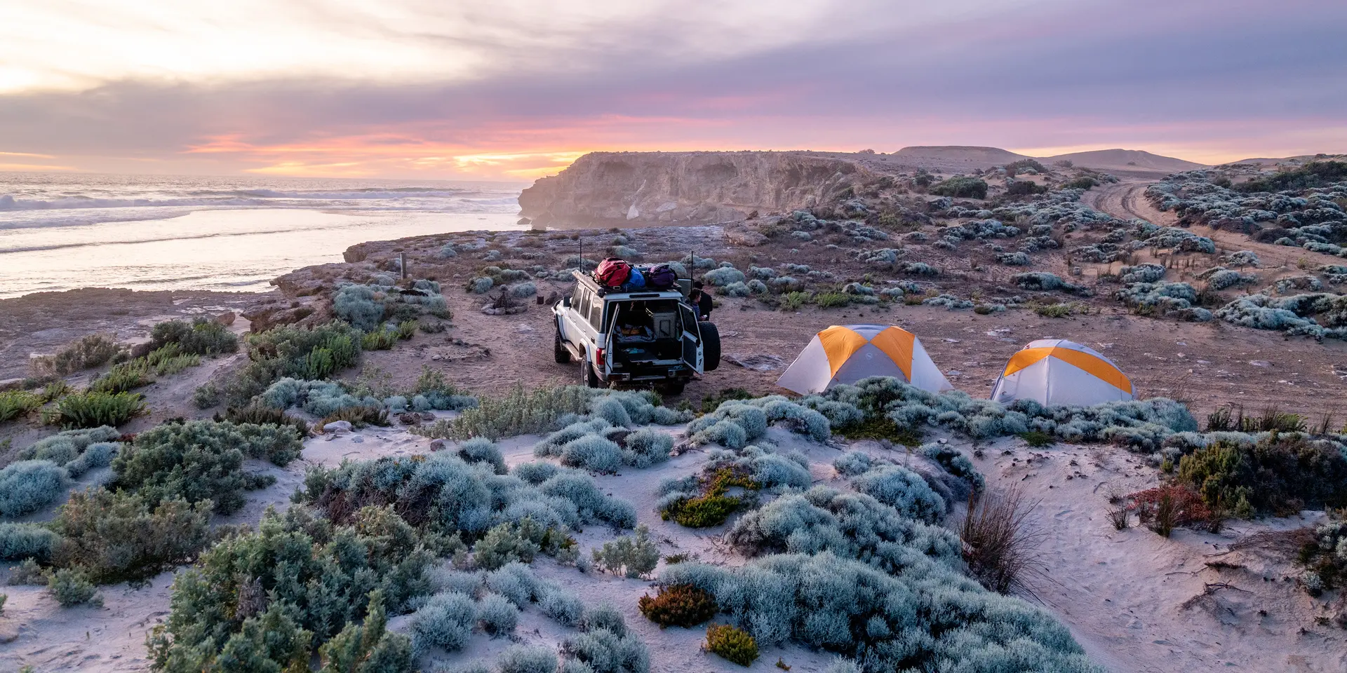 A jeep and two tents on a coast at sunset.