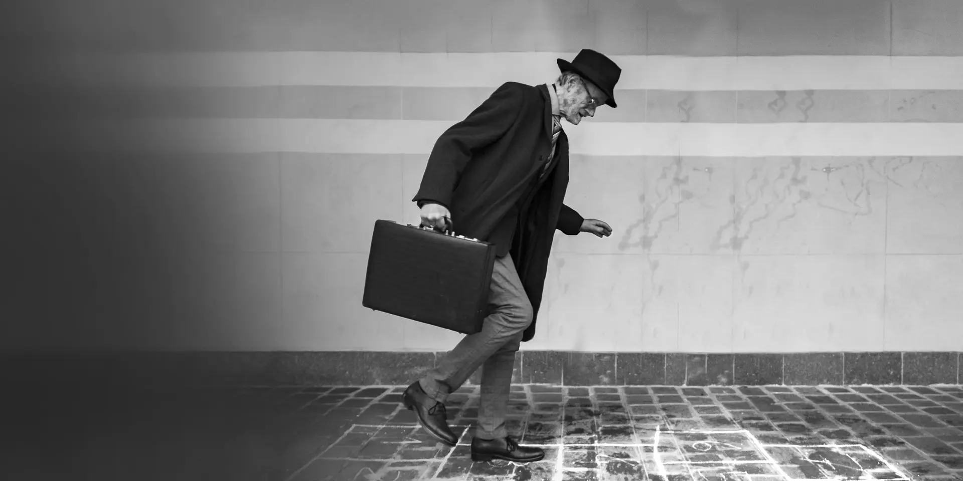 Elderly man in suit with hat and briefcase walking on icy cobblestones.