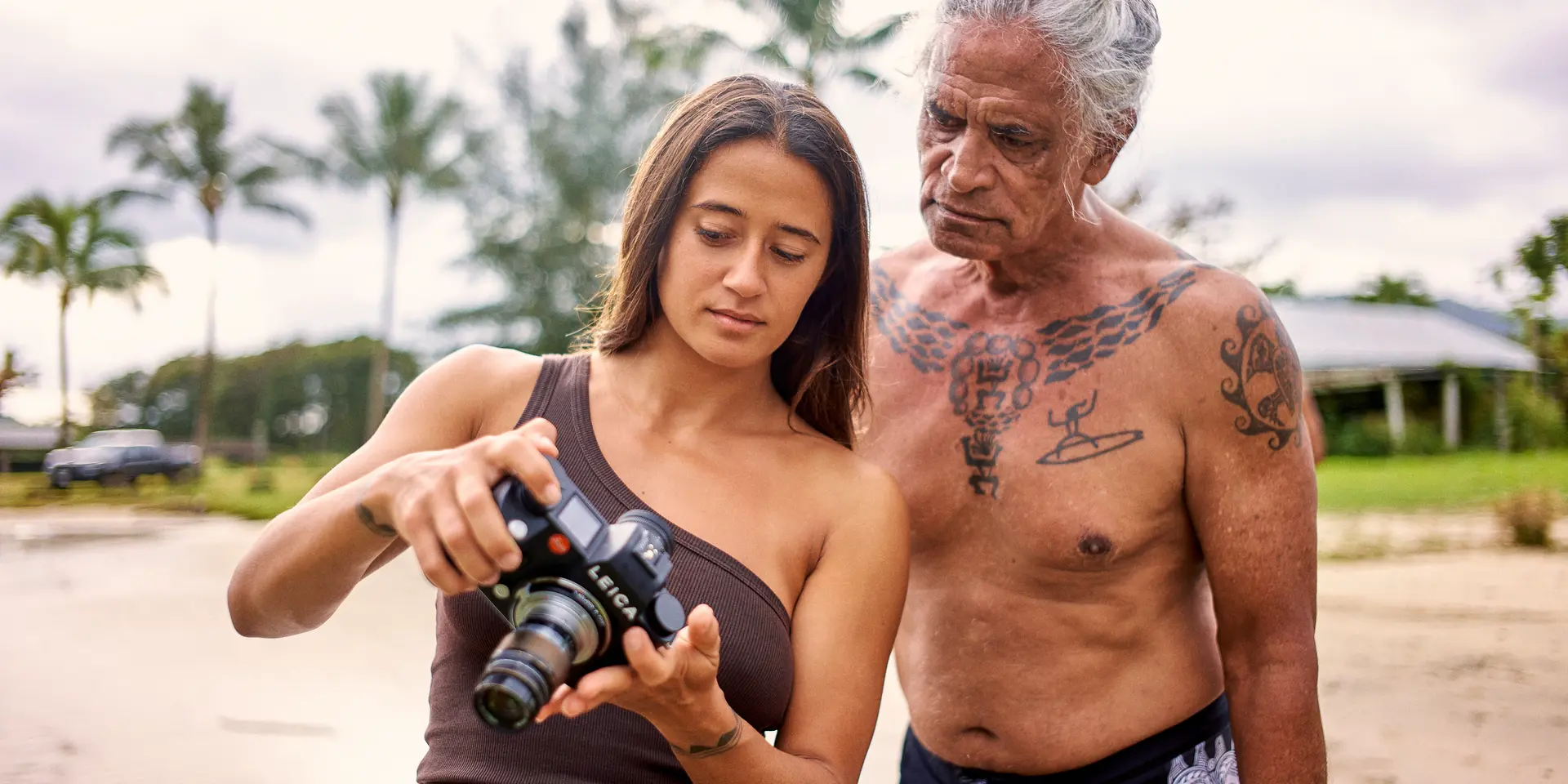 Mainei Kinimaka shows pictures on a camera to a man with Hawaiian tattoos on his upper body