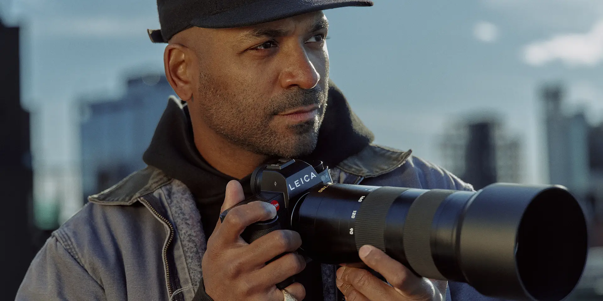 Close-up of a man holding a camera with skyscrapers in the background. 