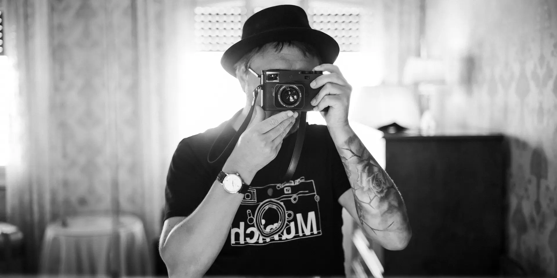 A person stands in a room and looks through a camera to take a photo.