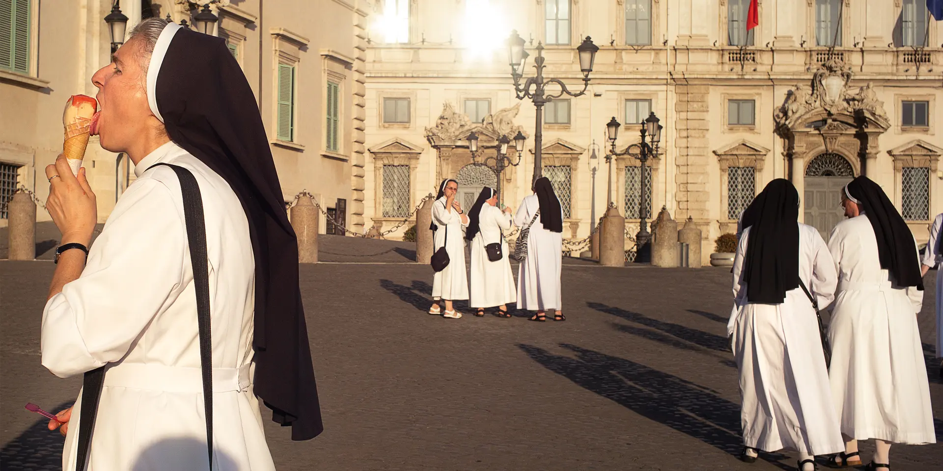 A nun eats an ice cream while several nuns talk in the background.