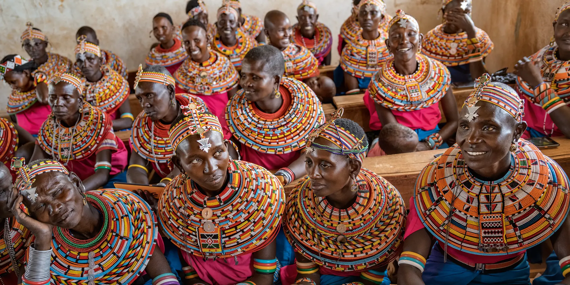 Women from the Samburu tribe in Kenya sitting on a wooden bench in traditional clothes and smiling.