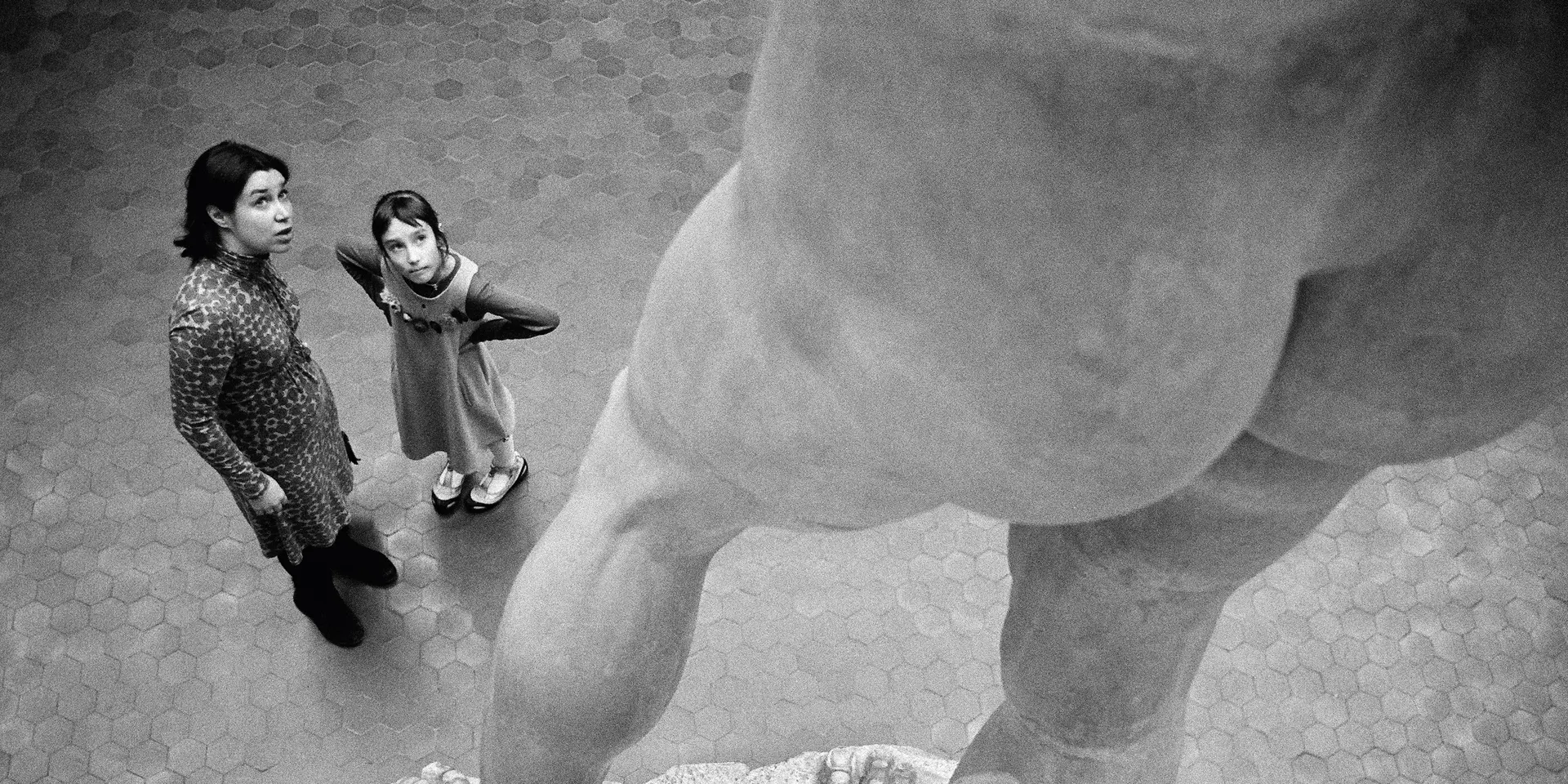 Two people stand in front of a large statue and look upwards.