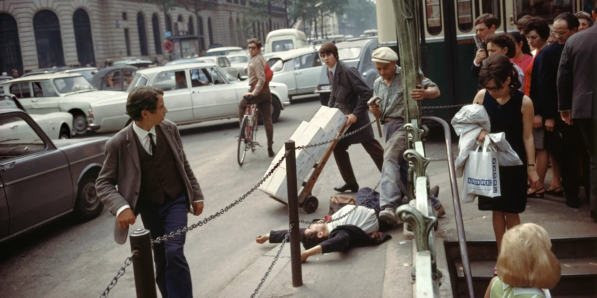 A young man in a suit and tie lies on his back with arms stretched above his head, directly next to the metro station