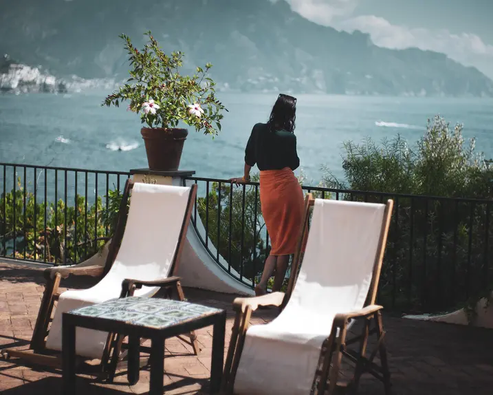 Woman on a large balcony with a view of a lake and mountains.