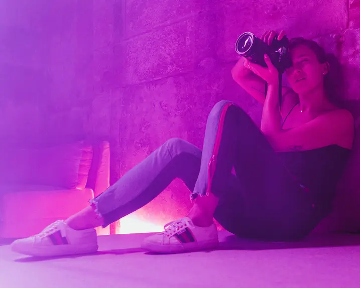 Alex Drewniak sits on the floor, taking pictures in a room lit by pink-purple light.