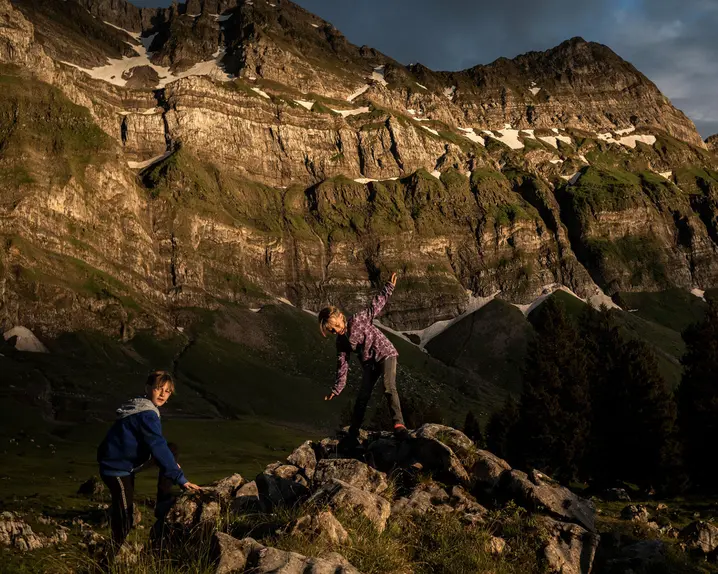 Two children climbing rocks in a mountain landscape at sunset.