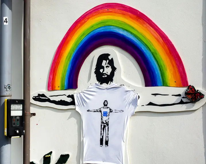 A mural on the wall of a man with outstretched arms in front of a rainbow.