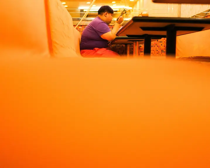 Close-up of an orange bench in a restaurant with a person sitting and eating in the background.