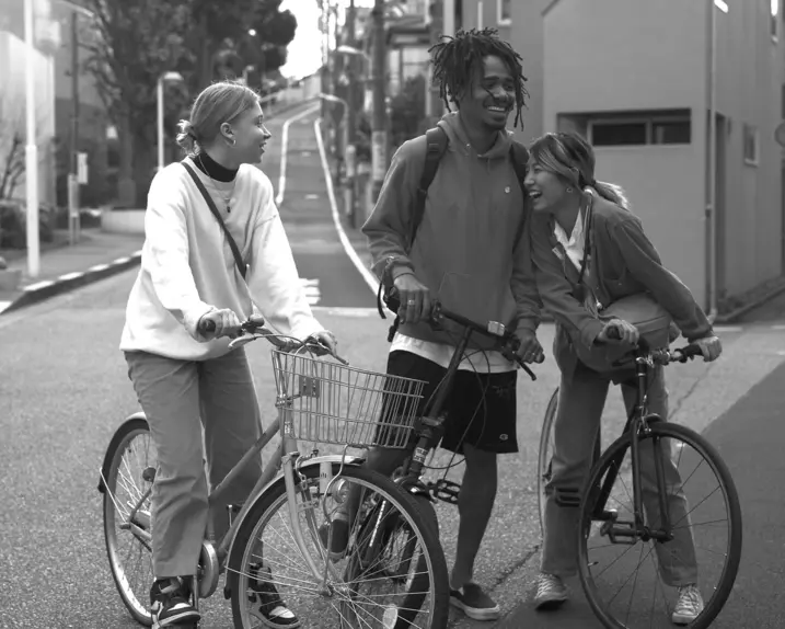 Three young people stand on bicycles in the street and laugh together.