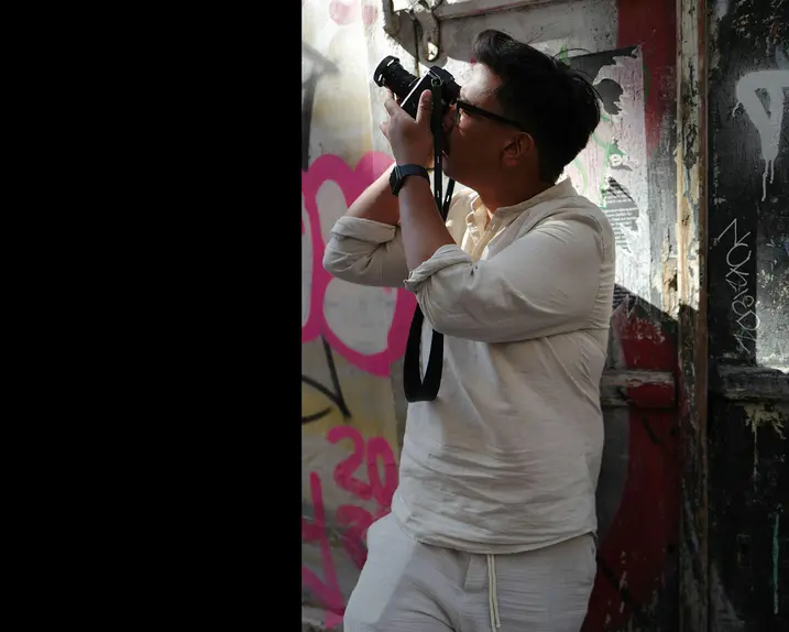 Patrick Domingo takes a photo standing in front of a graffiti wall.