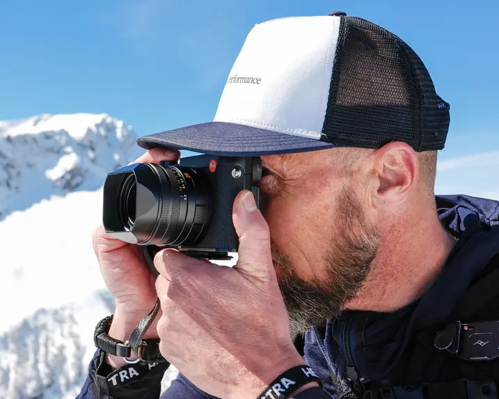 A man takes a photograph in a snowy mountain landscape.
