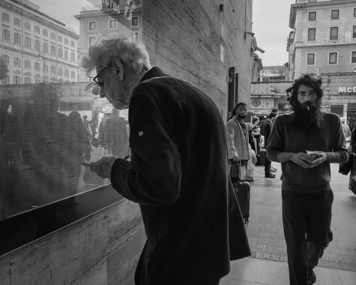 Elderly man in the city looking at a train timetable behind a pane of glass.